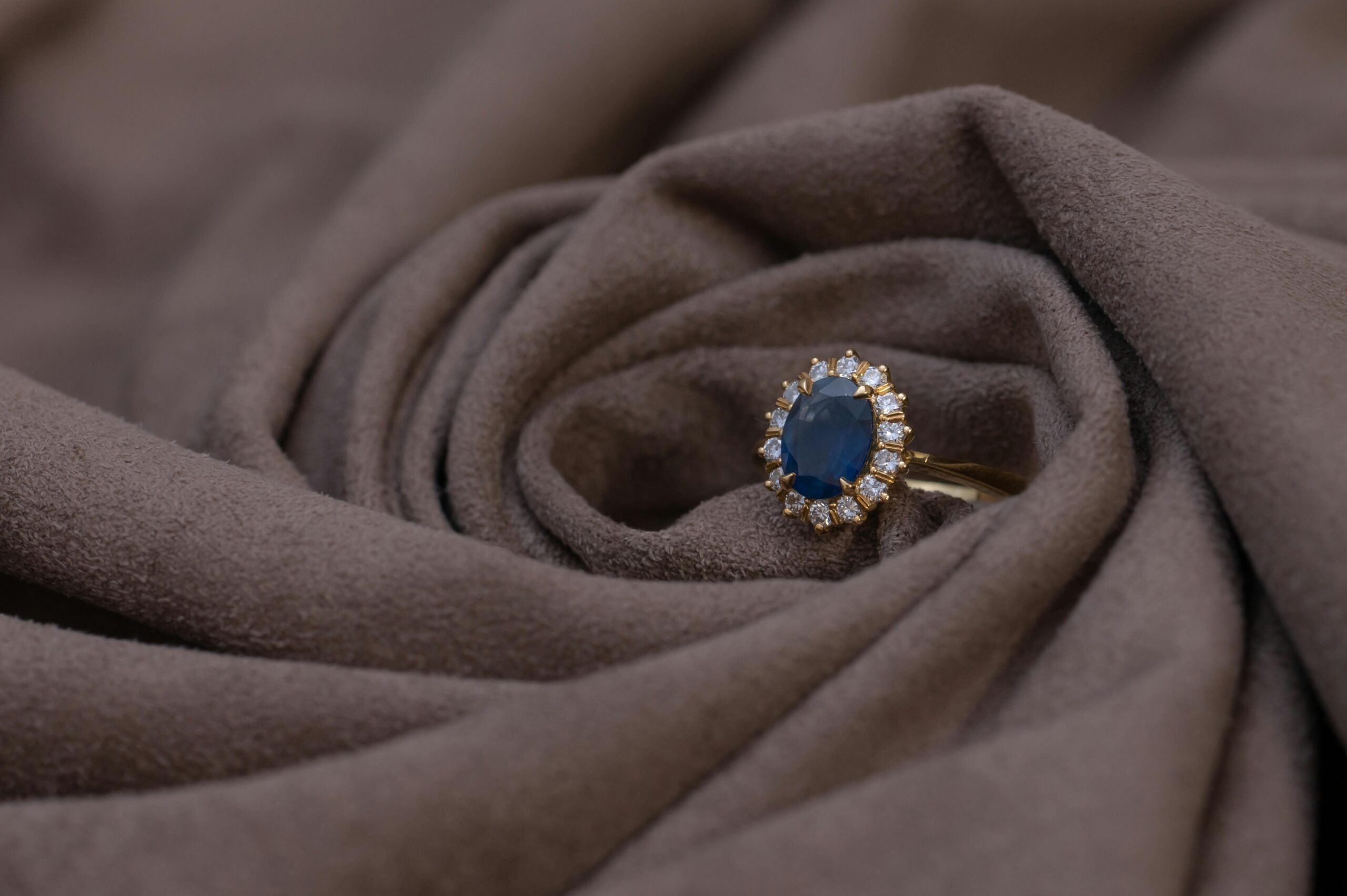 Close-up of a sapphire and diamond gold ring on brown suede, highlighting luxury jewelry details.